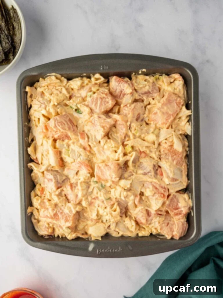 Assembled layers of rice, furikake, and salmon mixture in a baking pan, ready for the oven.