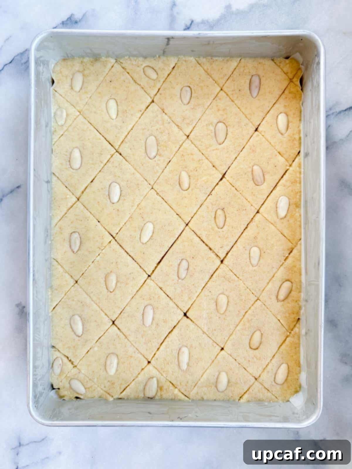 The Namoura recipe ready for baking, with its surface scored and each portion topped with a peeled almond half.