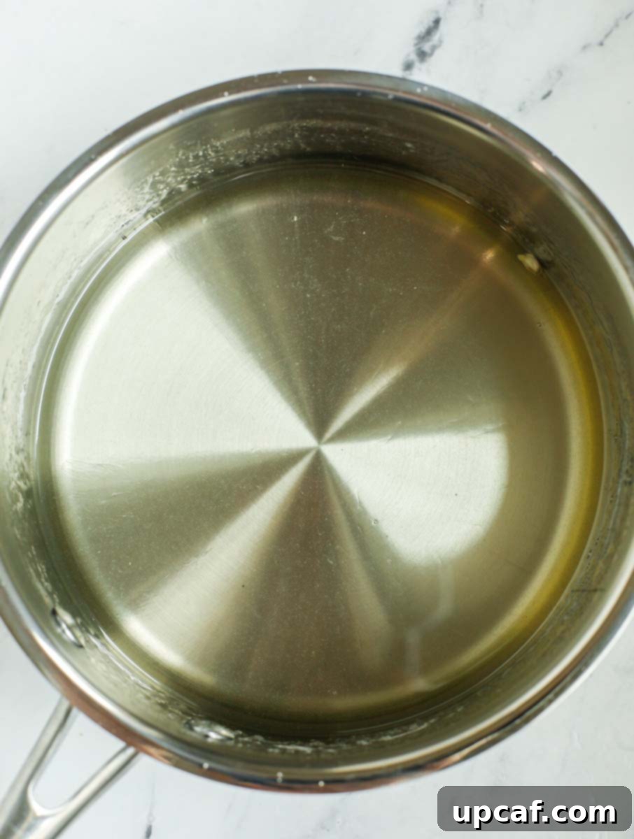 Clear, shimmering sugar syrup gently bubbling inside a saucepan, ready to be cooled and used.