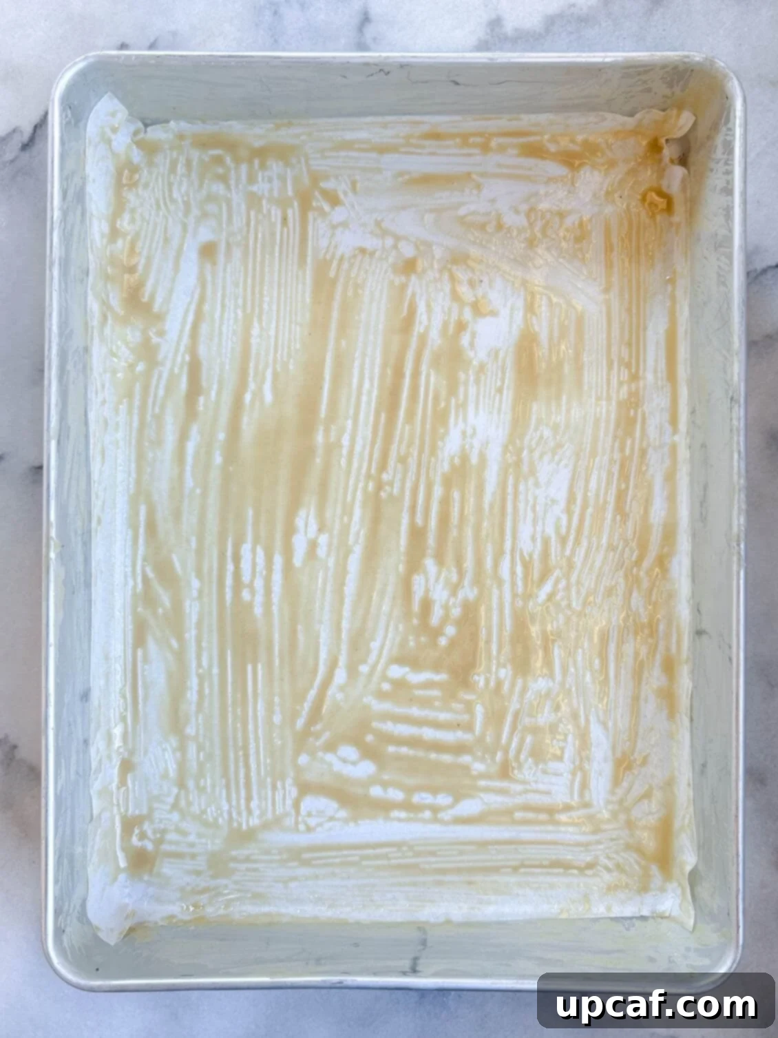 A baking pan prepared with parchment paper and brushed with tahini paste, ready for the Namoura batter.
