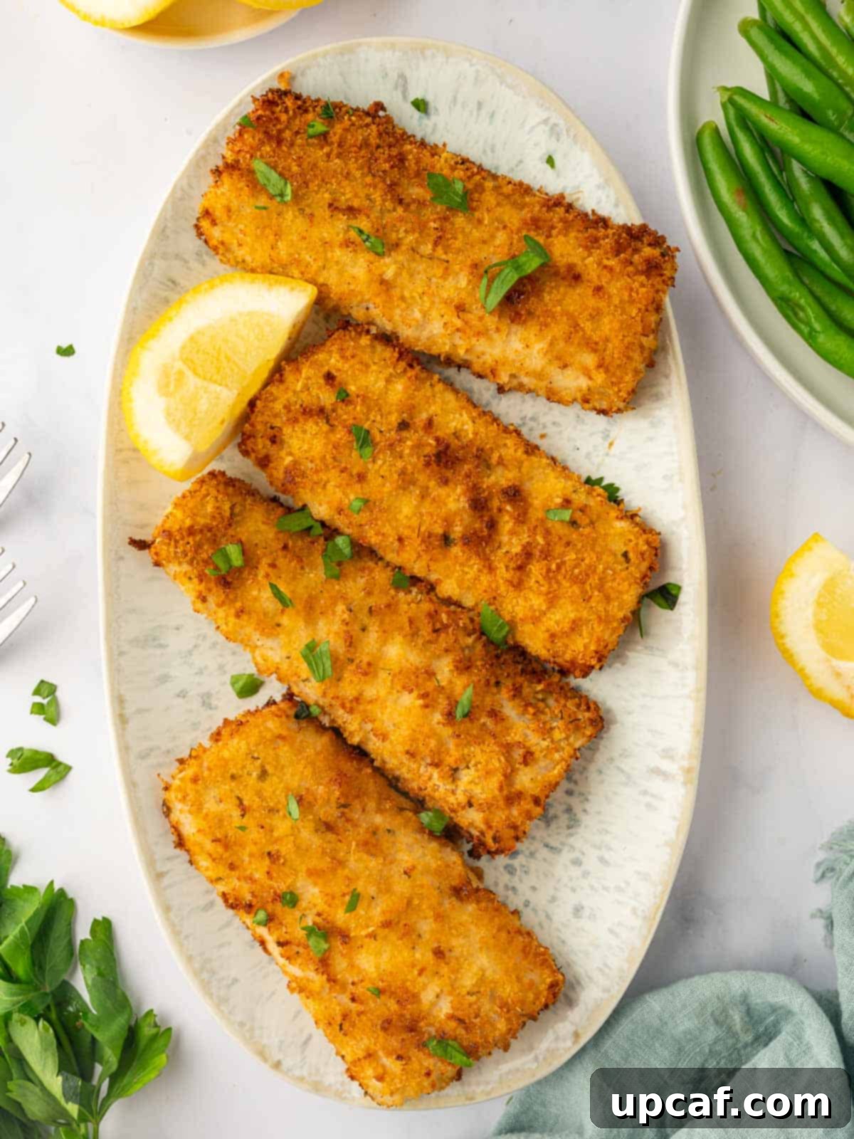 Four pieces of air-fried crispy mahi mahi fish served on a platter with fresh lemon wedges and garnished with vibrant parsley sprigs, ready to be enjoyed.