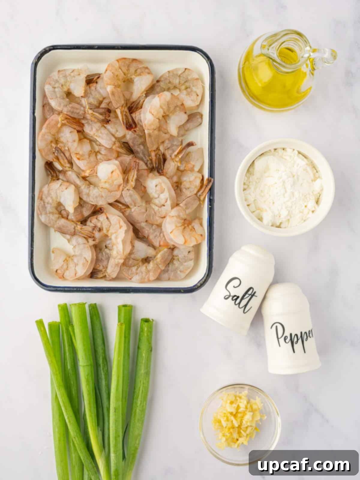 A curated selection of fresh ingredients laid out for making salt and pepper shrimp, including large shrimp, cornstarch, garlic, green onions, and spices.