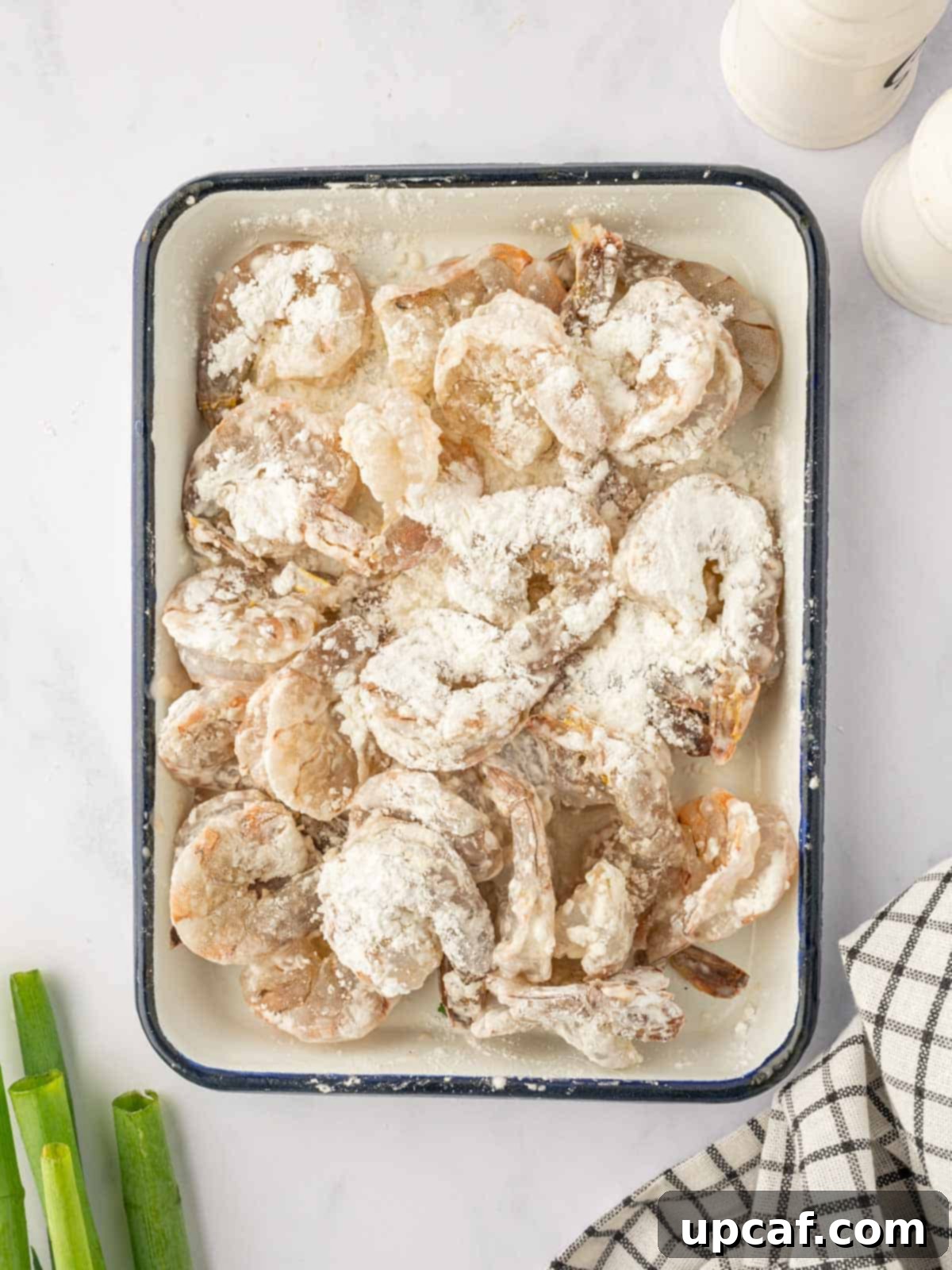 Raw shrimp being coated in a cornstarch and seasoning mixture, preparing them for frying.
