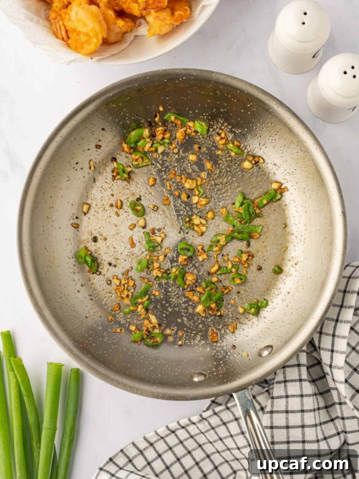 Garlic and green onions being sautéed in a skillet with salt and pepper, creating the aromatic base for the shrimp.