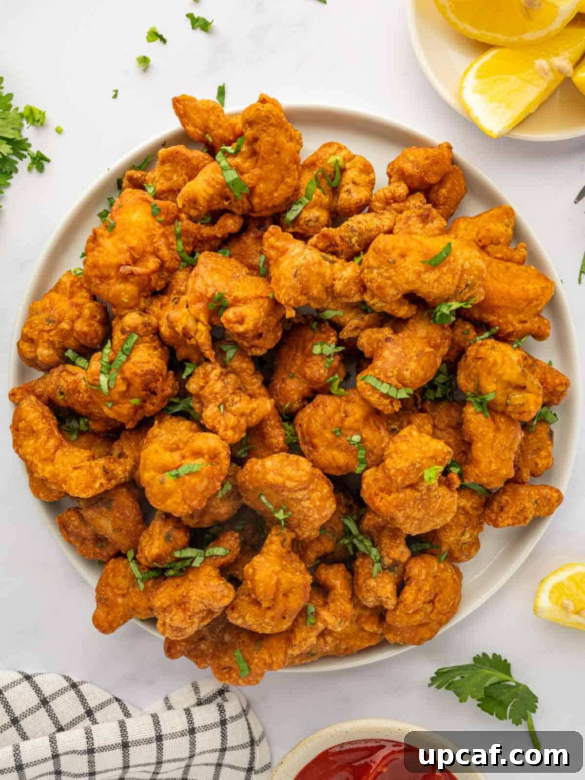 Golden Crispy Chicken Pakora 2 A large serving platter of golden, crispy chicken pakora garnished with cilantro and lemon wedges.