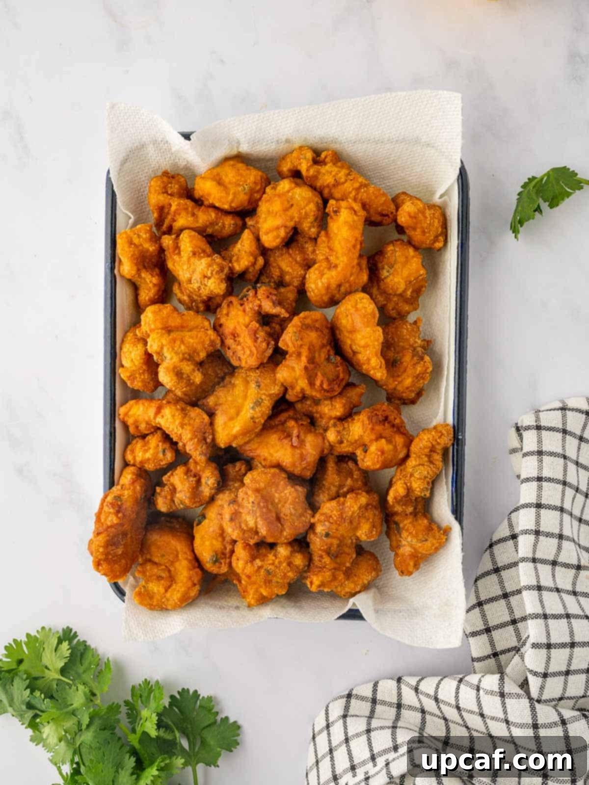 Golden Crispy Chicken Pakora 8 Freshly fried, golden chicken pakora bites are shown draining excess oil on a bed of paper towels on a wire rack.