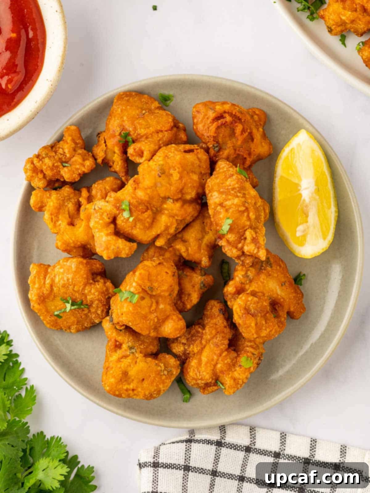 Golden Crispy Chicken Pakora 9 A plate of fried chicken pakora, expertly garnished with fresh lemon wedges, ready to be served.