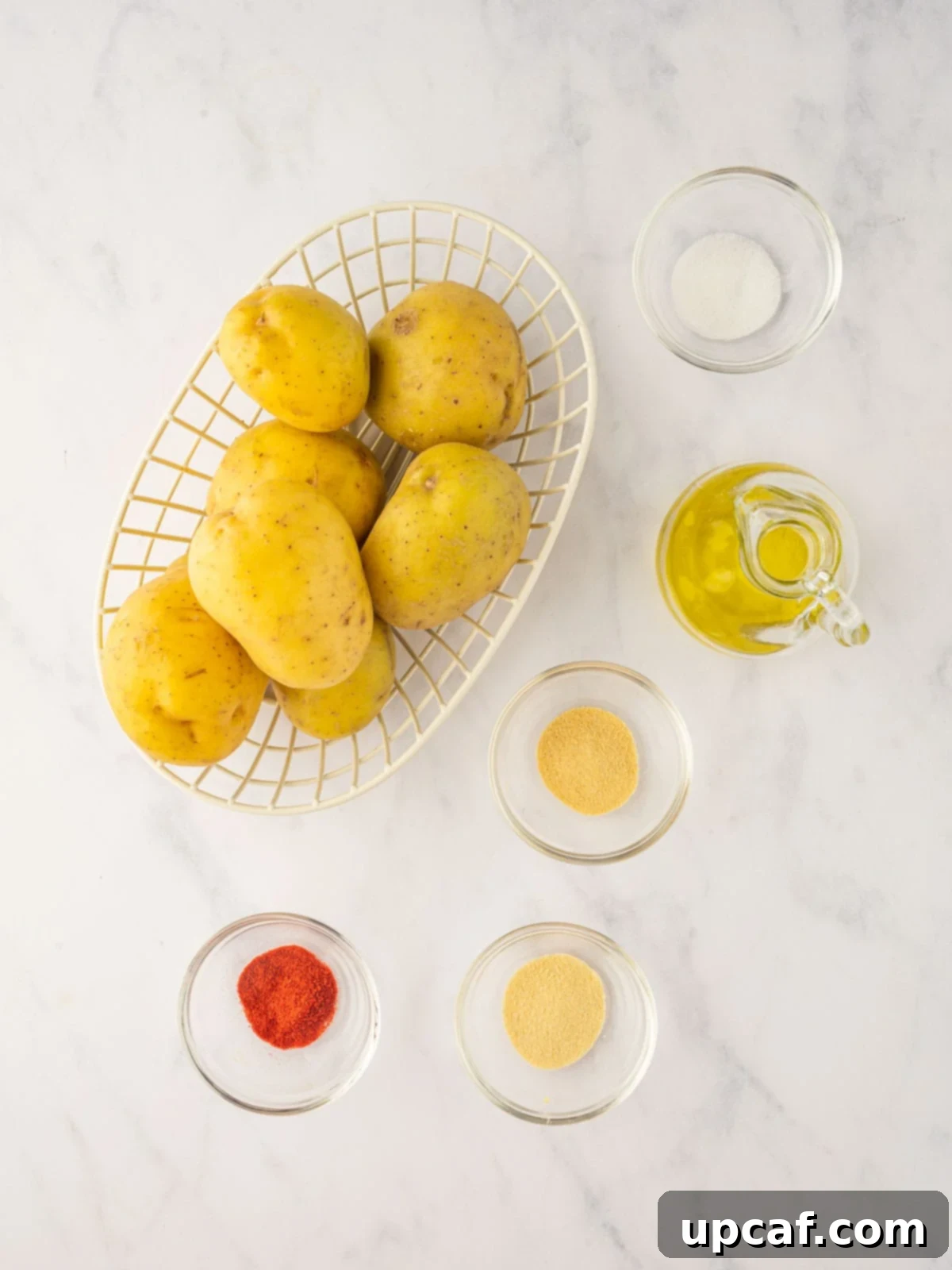 Golden Air-Fried Potato Coins 3 A bowl containing sliced potatoes, olive oil, and various spices arranged around it, illustrating the ingredients needed for crispy air fryer sliced potatoes.