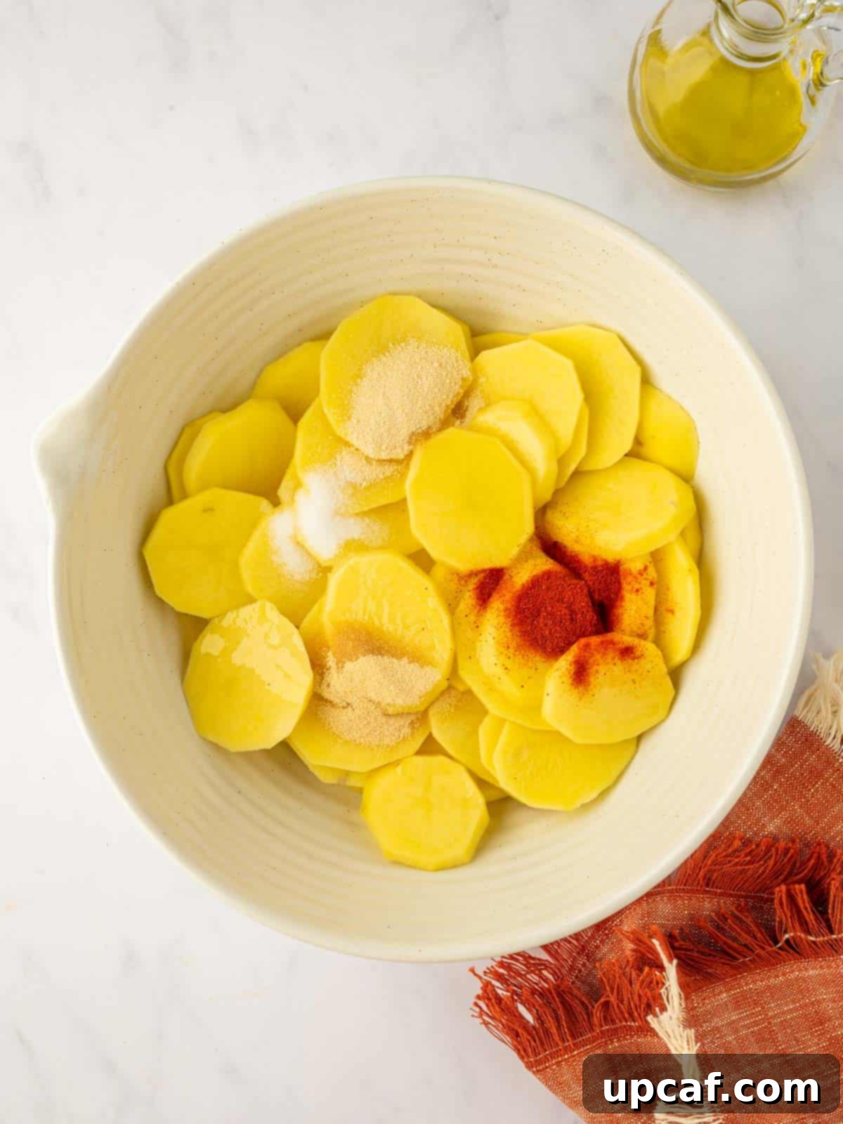 Golden Air-Fried Potato Coins 5 A hand sprinkling seasonings over sliced potatoes in a bowl.