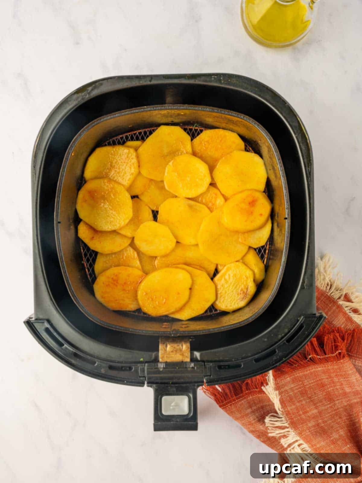 Golden Air-Fried Potato Coins 7 Seasoned potato slices being layered into an air fryer basket in a single layer.
