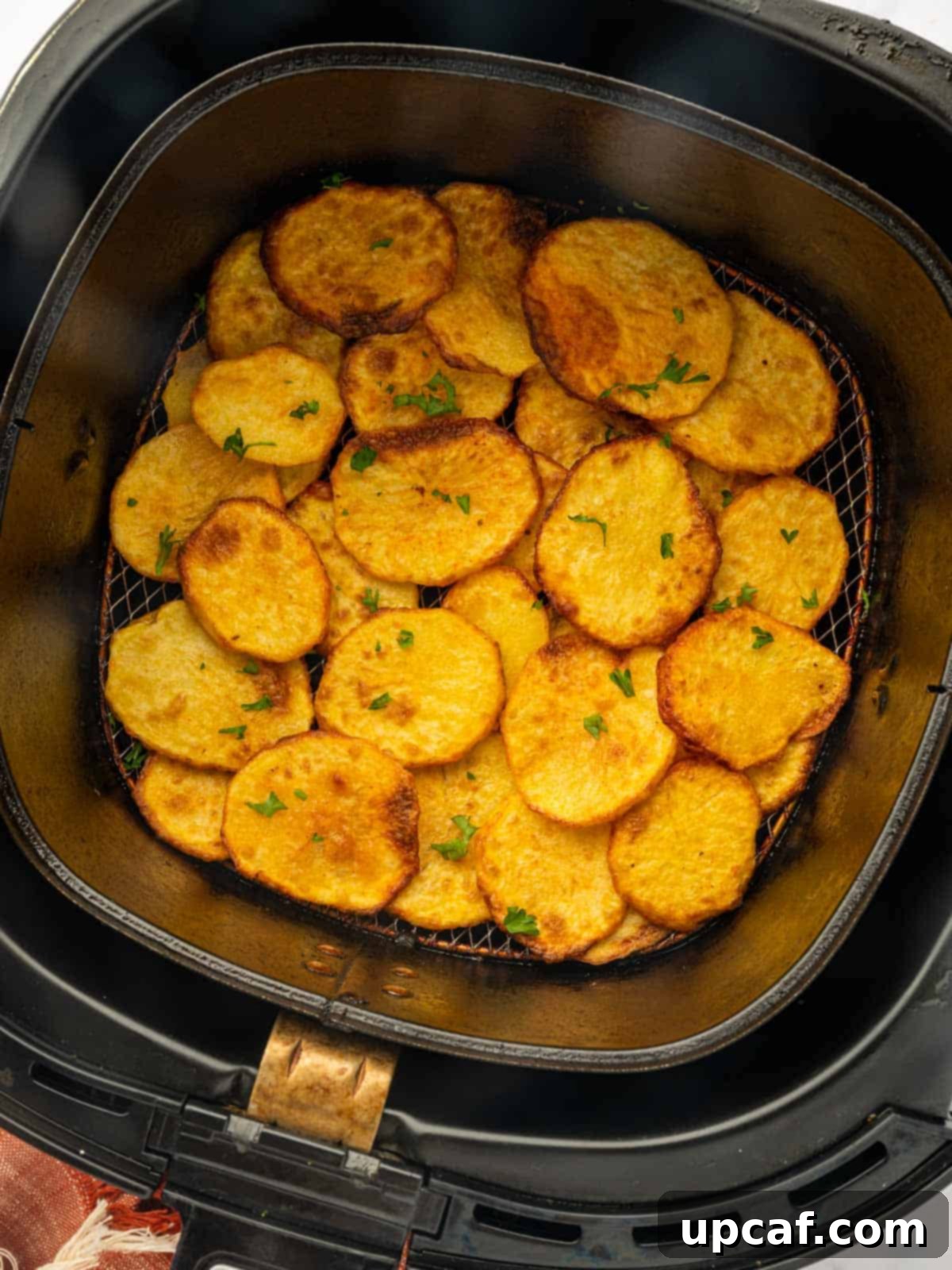 Golden Air-Fried Potato Coins 9 Crispy sliced potatoes in the air fryer basket, garnished with fresh parsley.