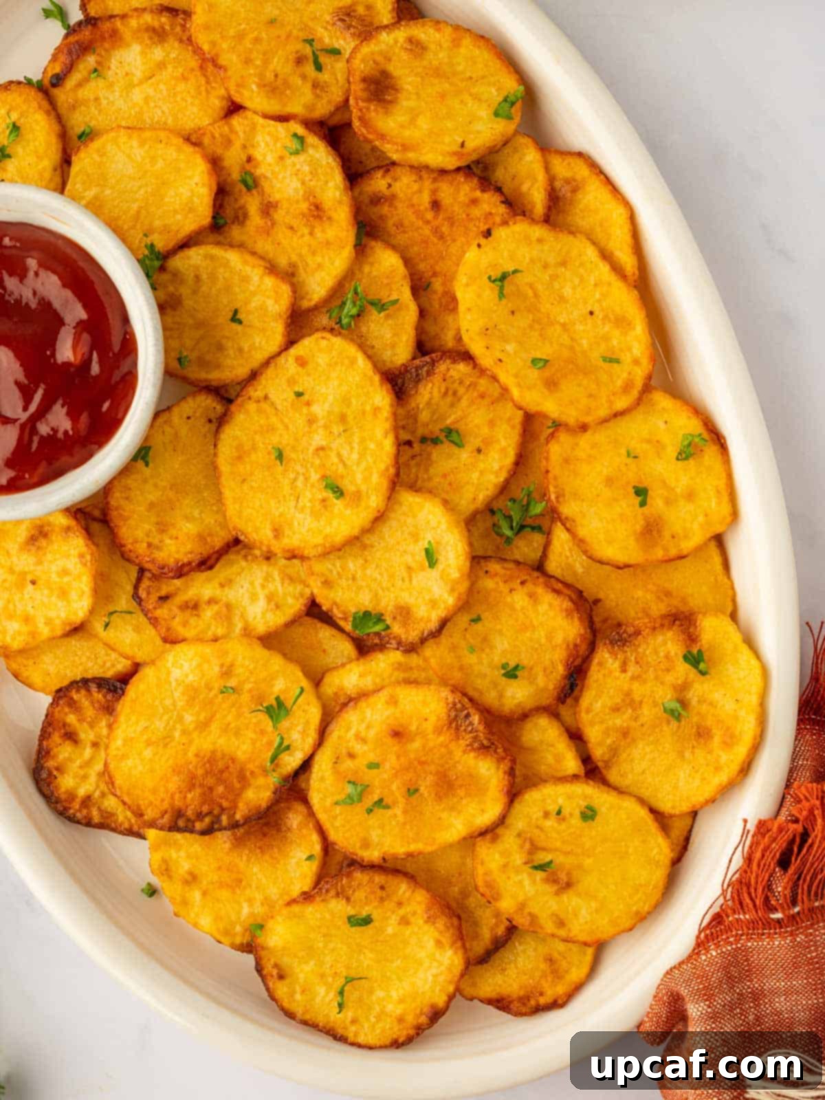Golden Air-Fried Potato Coins 10 Crispy potato chips are piled high on a platter, with a small dish of ketchup for dipping.