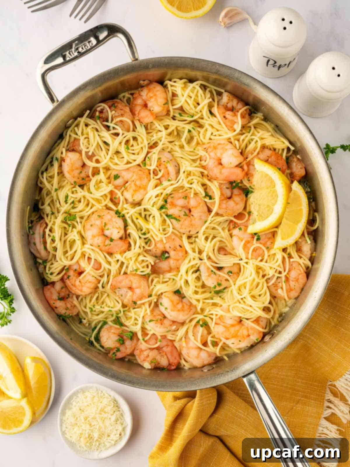 Pasta with shrimp and lemon wedges in a skillet.