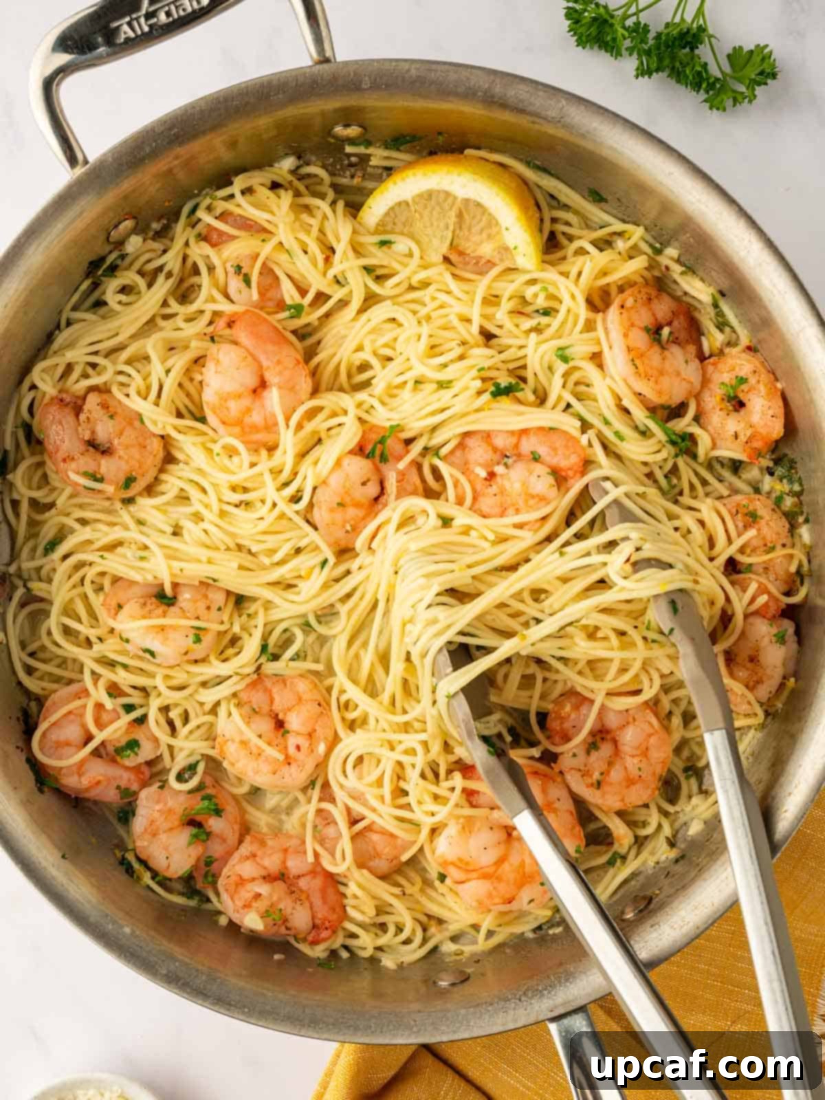 Tongs lift a portion of angel hair pasta from a skillet.