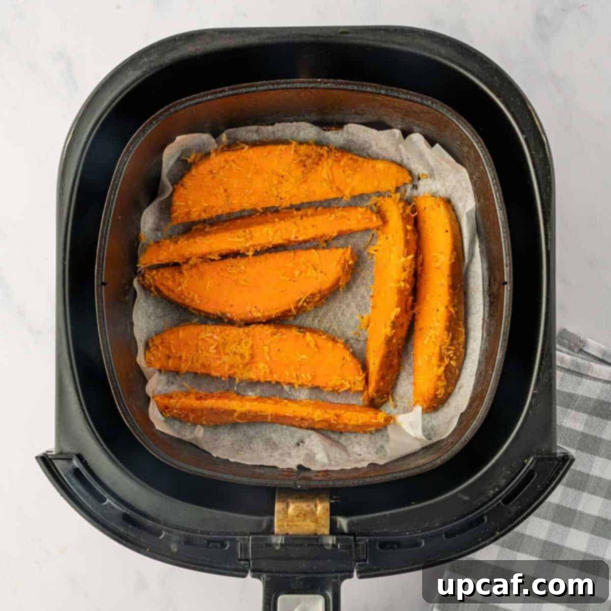 Parmesan coated sweet potatoes in an air fryer basket.
