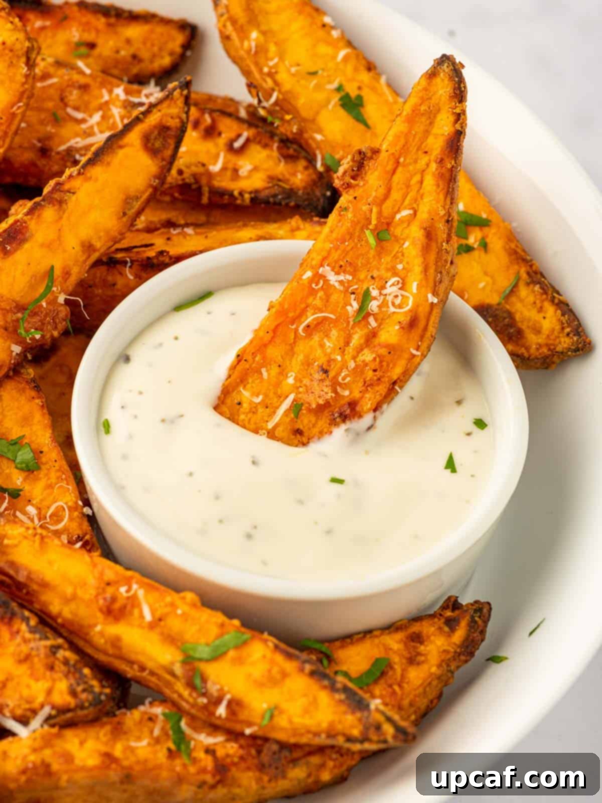 A sweet potato is dipped into a dish of sauce.