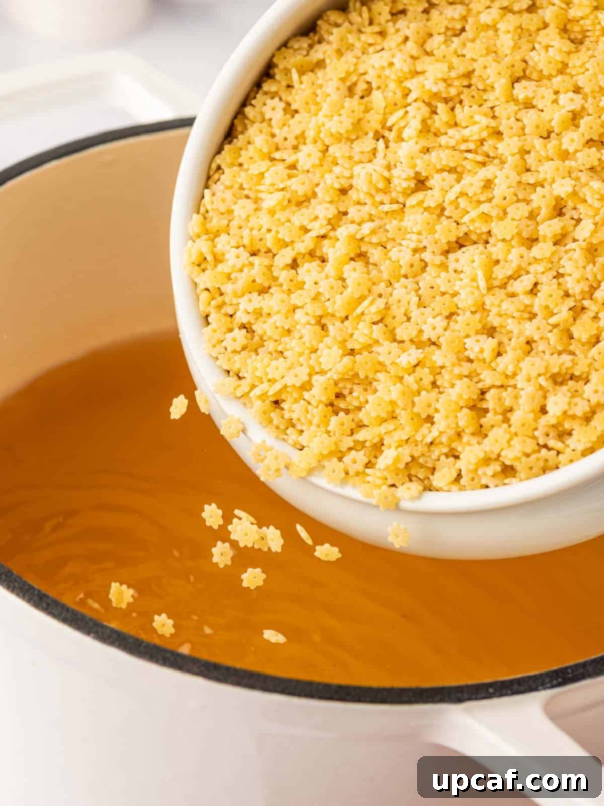 Stelline pasta is added to hot chicken broth in a dutch oven.