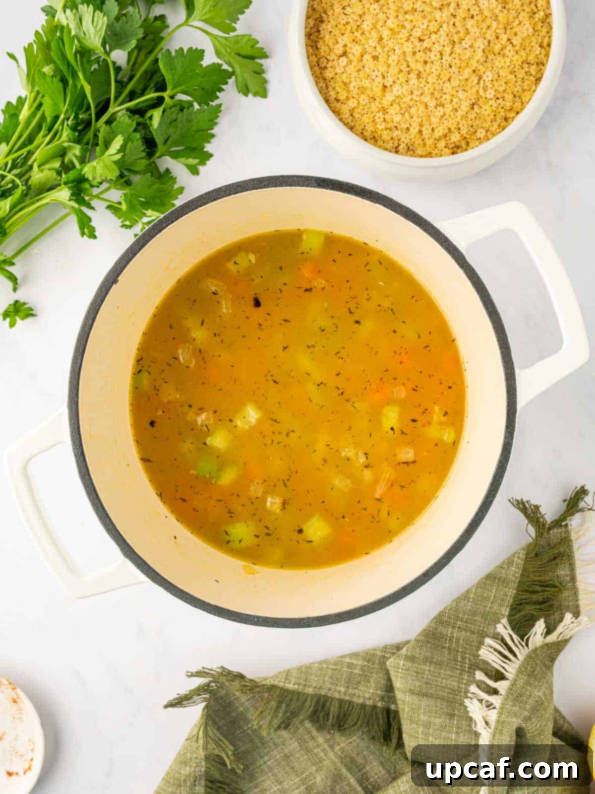 Comforting Italian Pastina Soup 6 Chicken broth and vegetables simmering in a Dutch oven with herbs and spices.