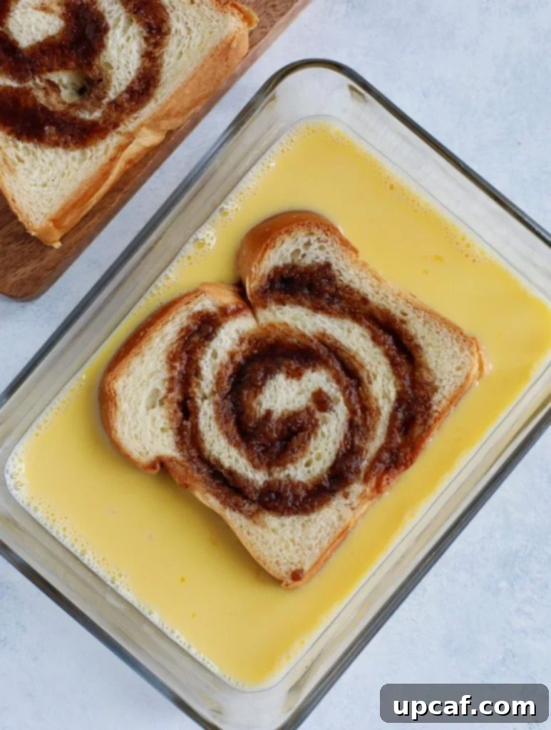 Marbled Cinnamon French Toast 3 A slice of brioche bread, enriched with a cinnamon swirl, being dipped into a shallow dish filled with egg wash.