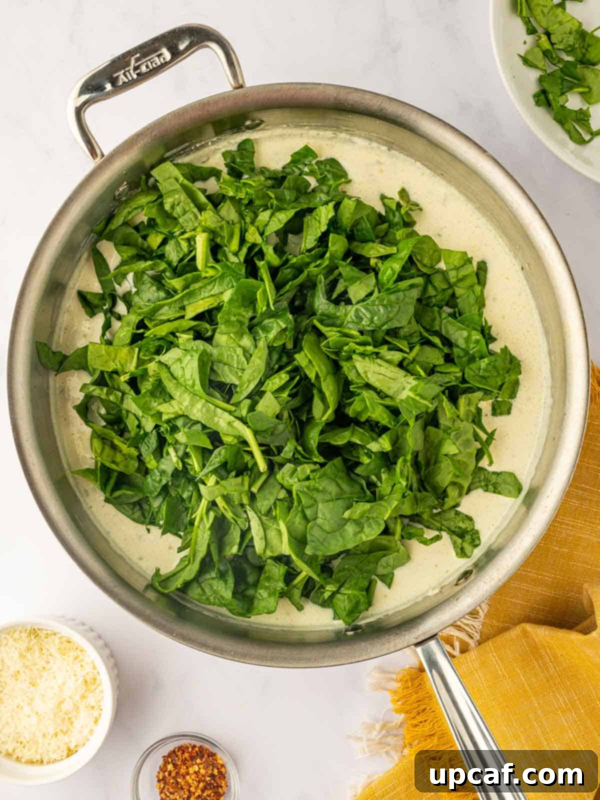 Fresh spinach wilting gracefully into the rich, creamy Boursin cheese sauce in a skillet, adding color and nutrients.