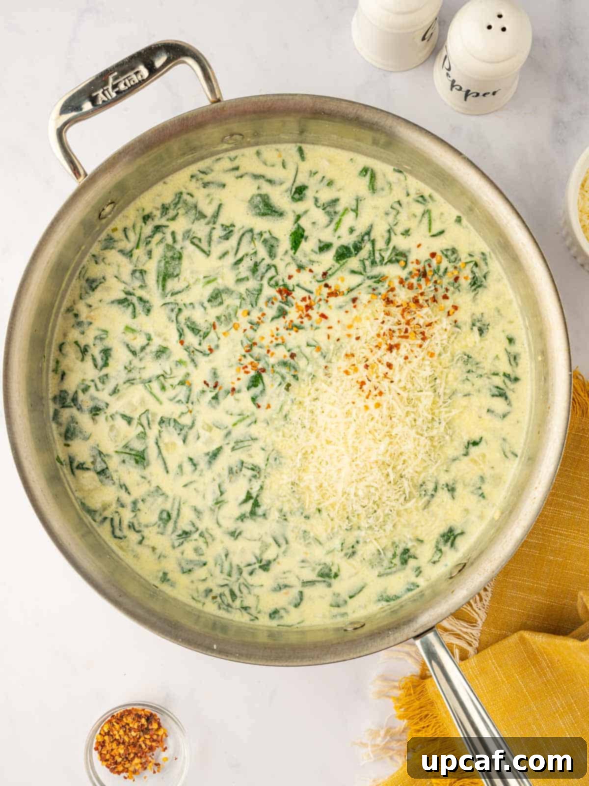 Grated Parmesan cheese and crushed red pepper flakes being stirred into the fragrant Boursin cheese sauce.