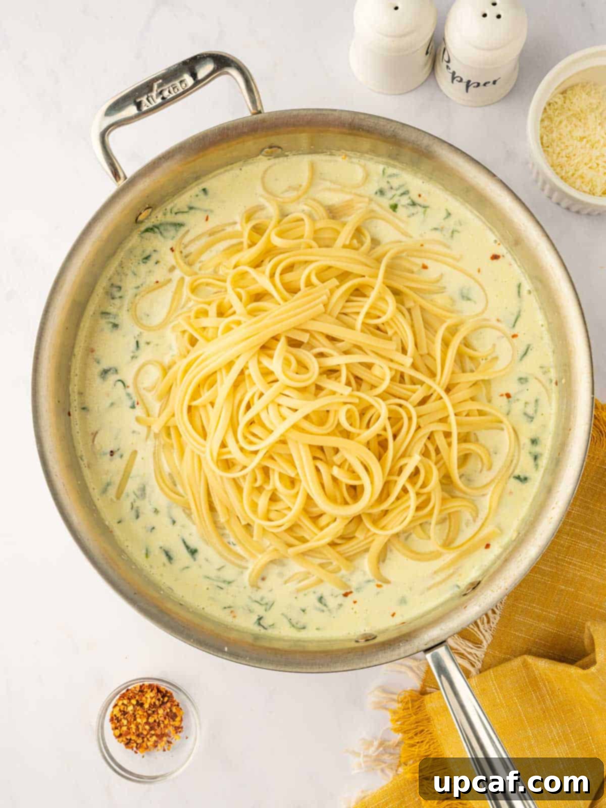 Cooked linguine pasta being tossed generously into the rich, creamy Boursin cheese sauce in a large skillet.