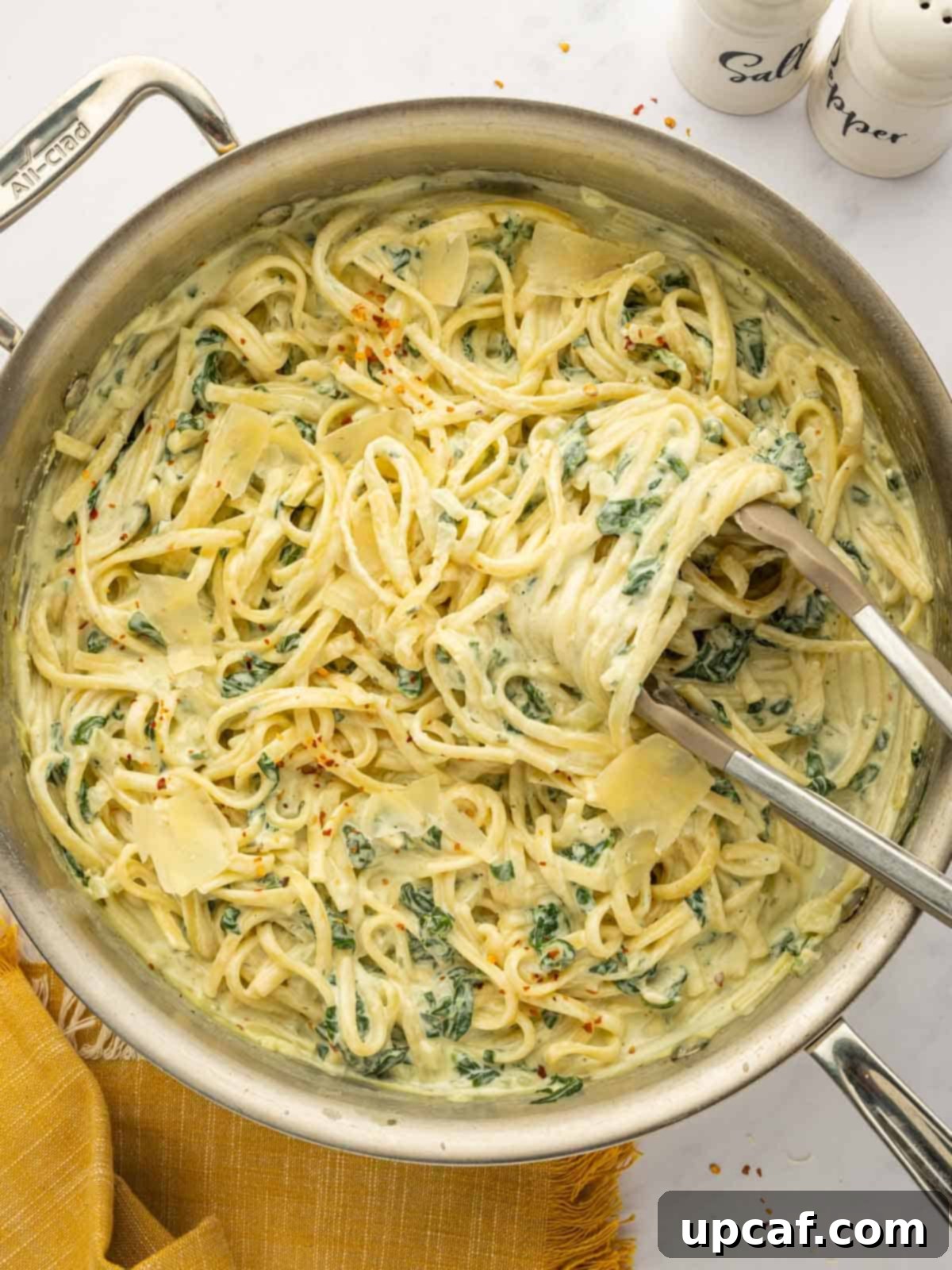 Kitchen tongs tossing a generous portion of Boursin cheese pasta in a large skillet, ready for serving.
