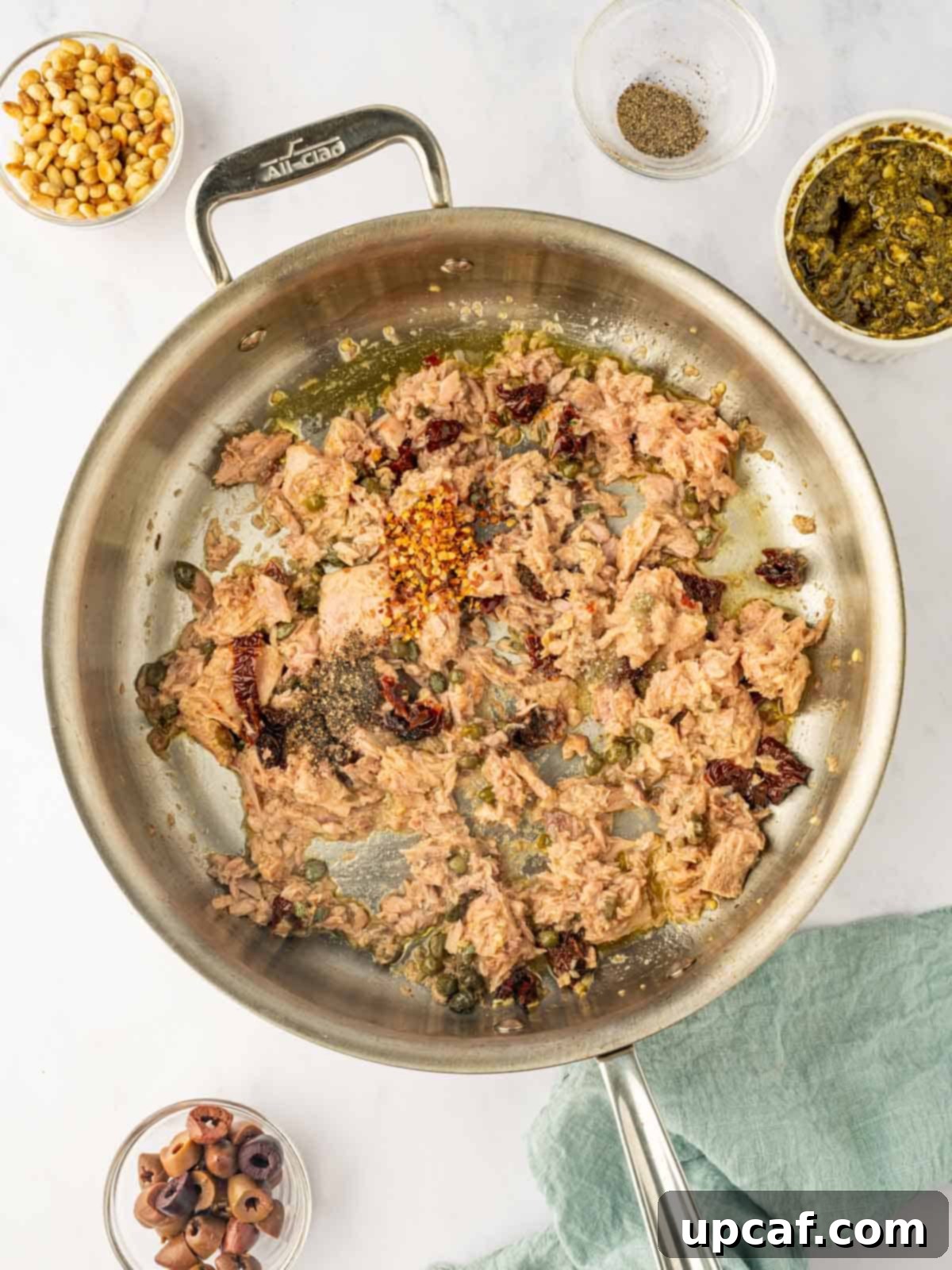 Mediterranean Tuna Pesto Pasta 5 Canned tuna being broken up and sautéed in a skillet with the caper and sun-dried tomato mixture, seasoned with red pepper flakes.