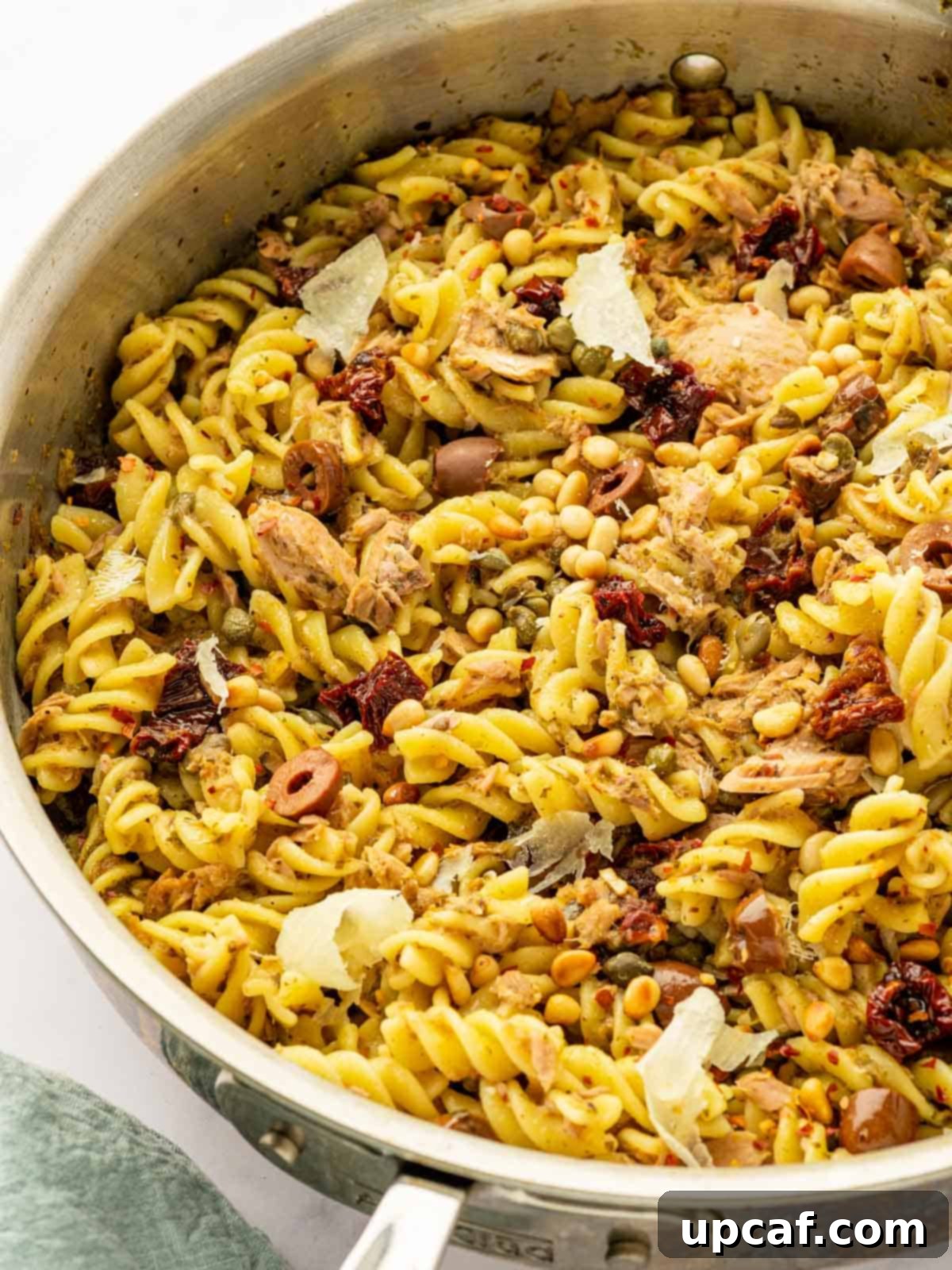 Mediterranean Tuna Pesto Pasta 7 A large skillet filled with tuna pesto pasta, garnished generously with shaved Parmesan cheese and fresh basil leaves, ready to be served.