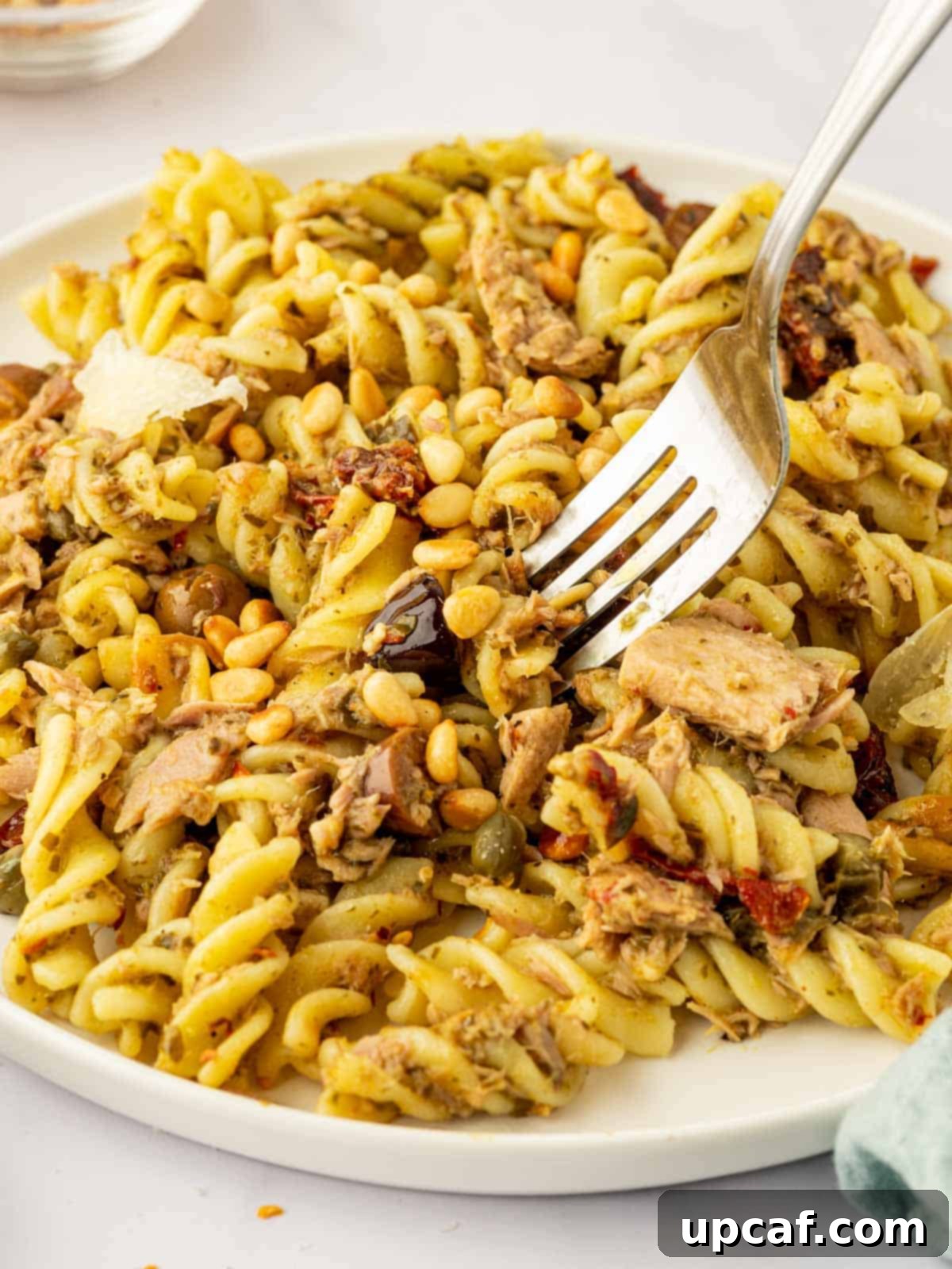 Mediterranean Tuna Pesto Pasta 8 A fork lifts a generous bite of tuna pesto pasta, showing the intertwining strands of pasta, tuna flakes, and green pesto sauce.
