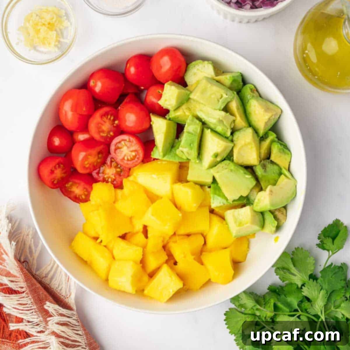 A bowl filled with diced avocado, sweet mangoes, and juicy cherry tomatoes, prepped for the salad.
