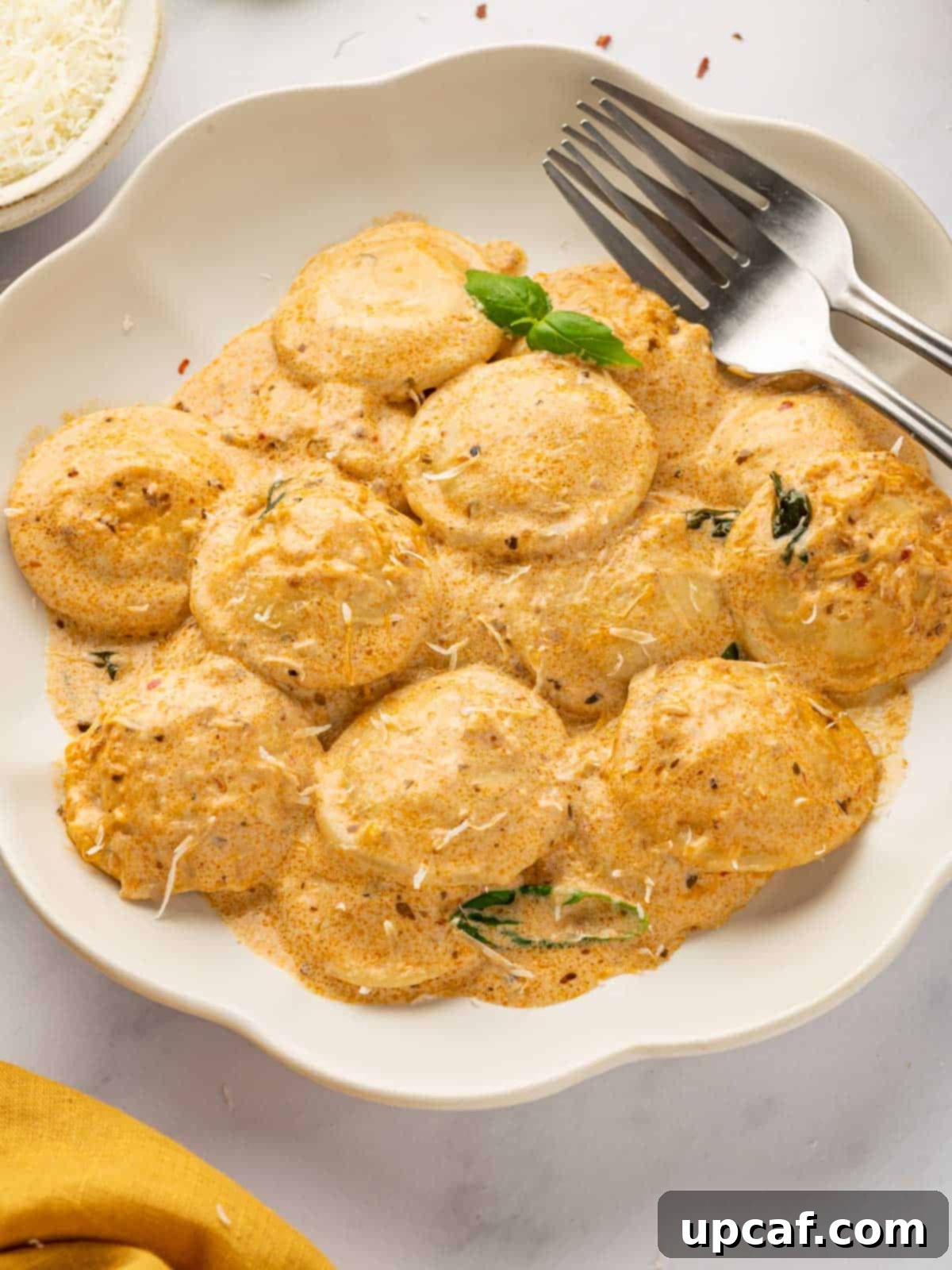 A fork rests beside a plate of ravioli topped with a creamy red sauce, garnished with fresh herbs.