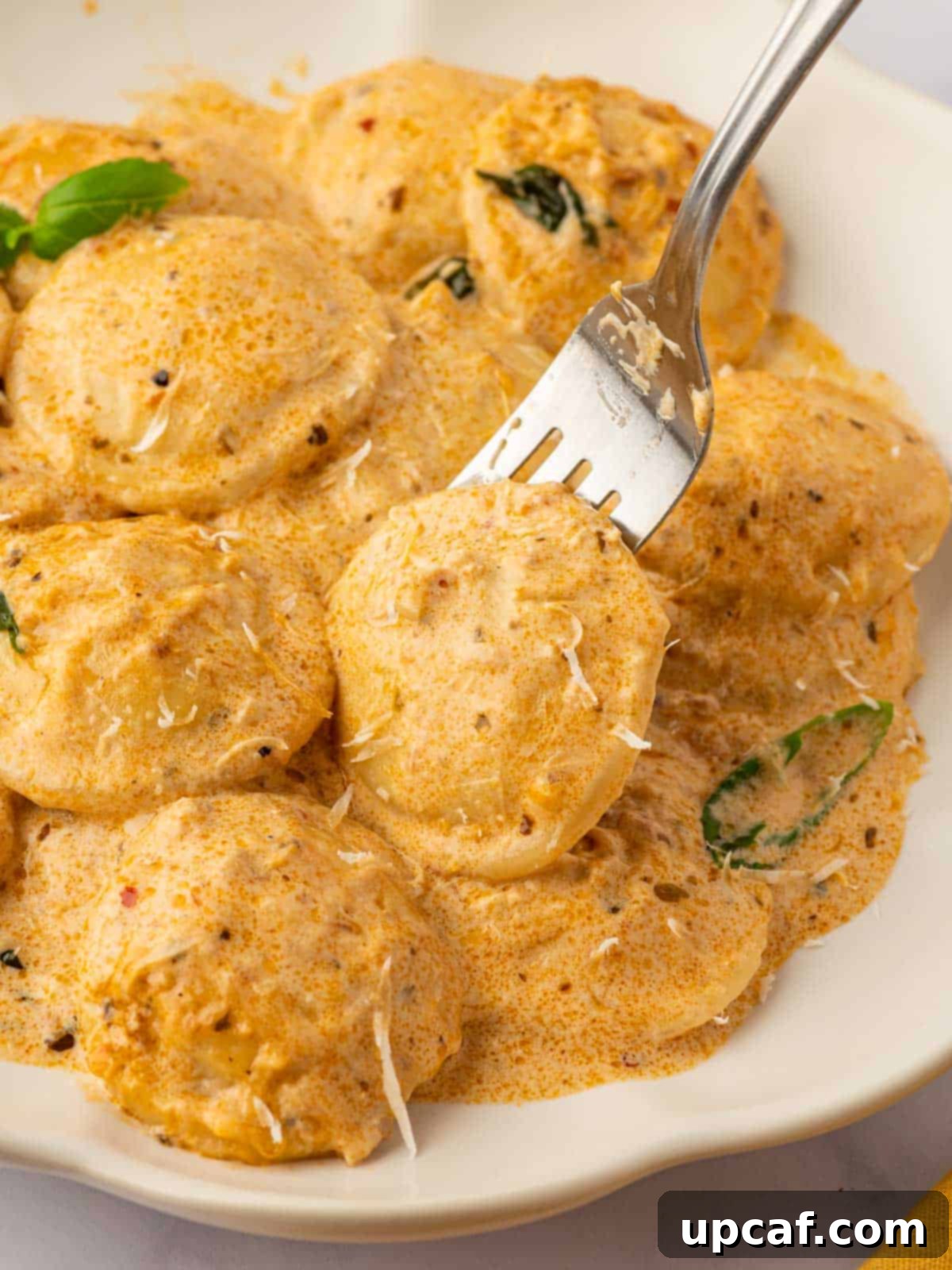 A fork lifting a single piece of delicious sun-dried tomato ravioli, coated in creamy sauce and garnished with fresh herbs, showcasing its appetizing texture.