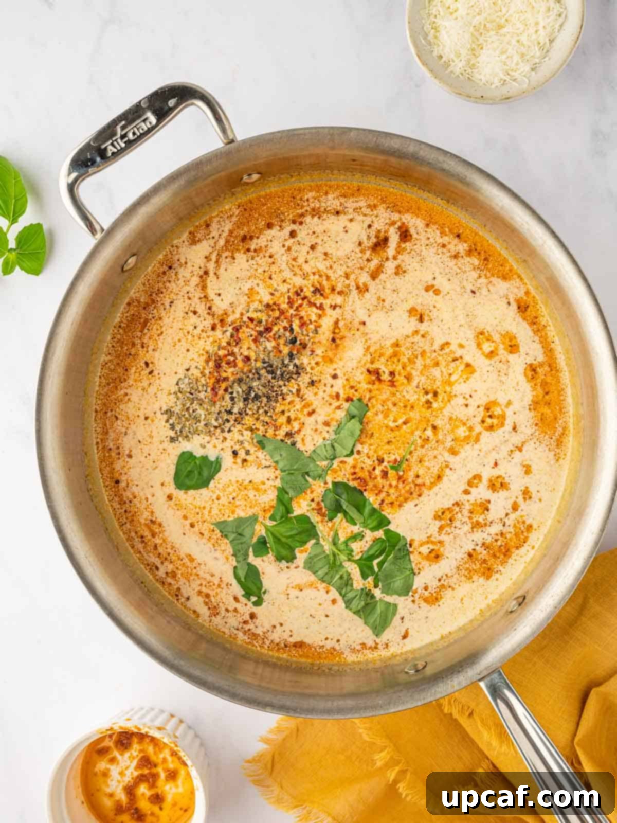 Fresh basil leaves, oregano, and red pepper flakes added to a simmering creamy tomato sauce for seasoning.
