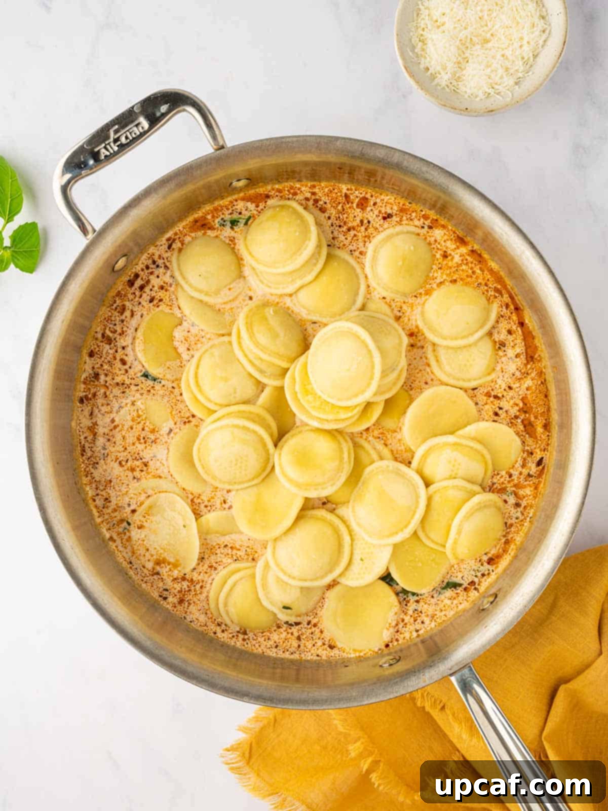 Cooked four cheese ravioli being gently added to the creamy sun-dried tomato pesto sauce in a large skillet.