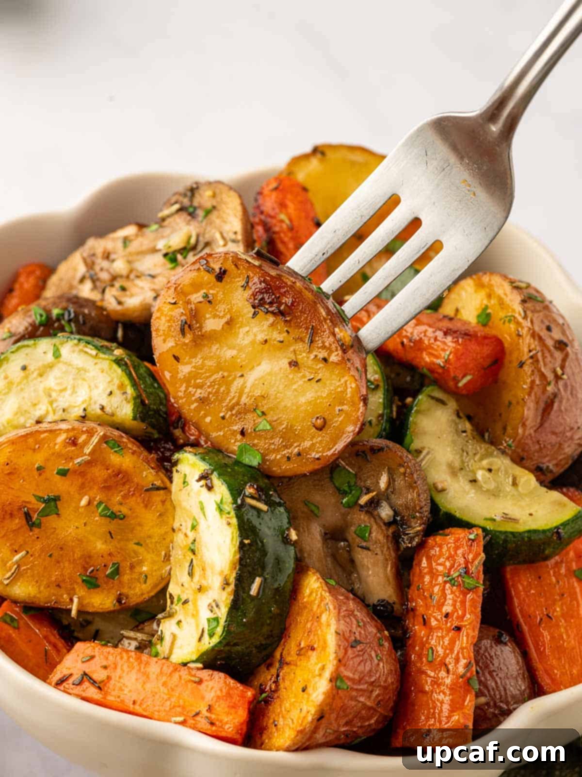 A fork picks up a roasted potato from a bowl of roasted vegetables, highlighting the tender interior.