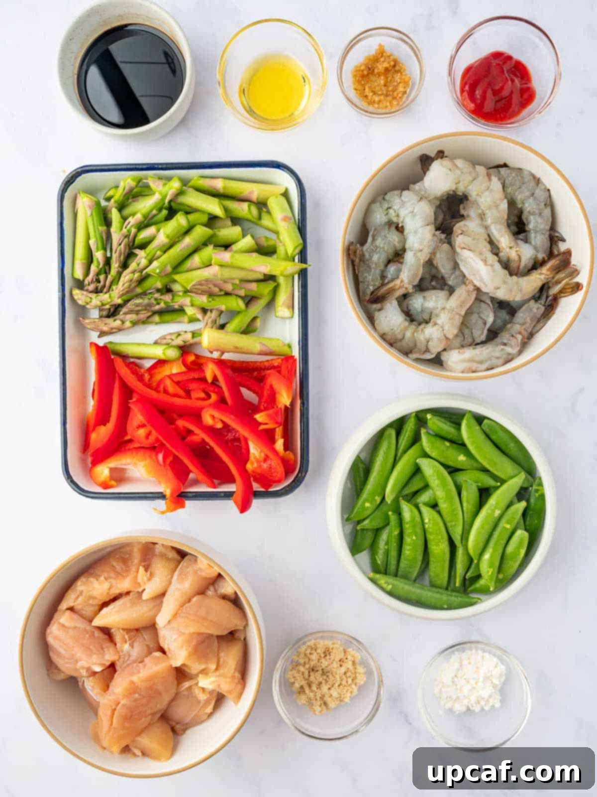 Surf and Turf Stir Fry 3 Fresh ingredients like chicken, shrimp, red bell pepper, asparagus, snow peas, and sauce components laid out for stir fry preparation.