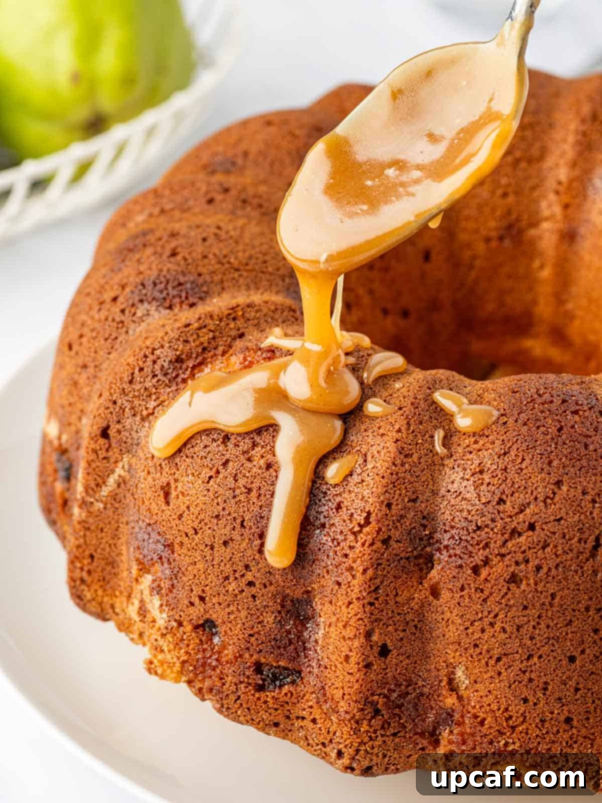 A spoon drizzles caramel on a cooled bundt cake.