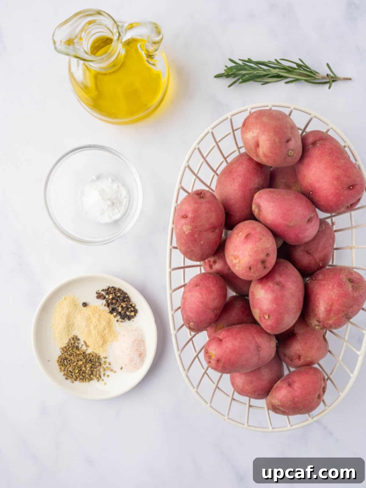 A spread of fresh ingredients including baby potatoes, olive oil, and various spices, ready to make roasted baby potatoes.