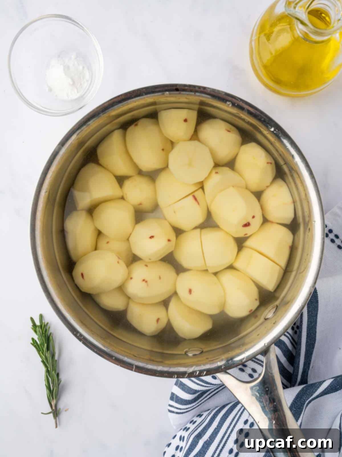 Baby potatoes are being boiled in salted water with baking soda, releasing steam.