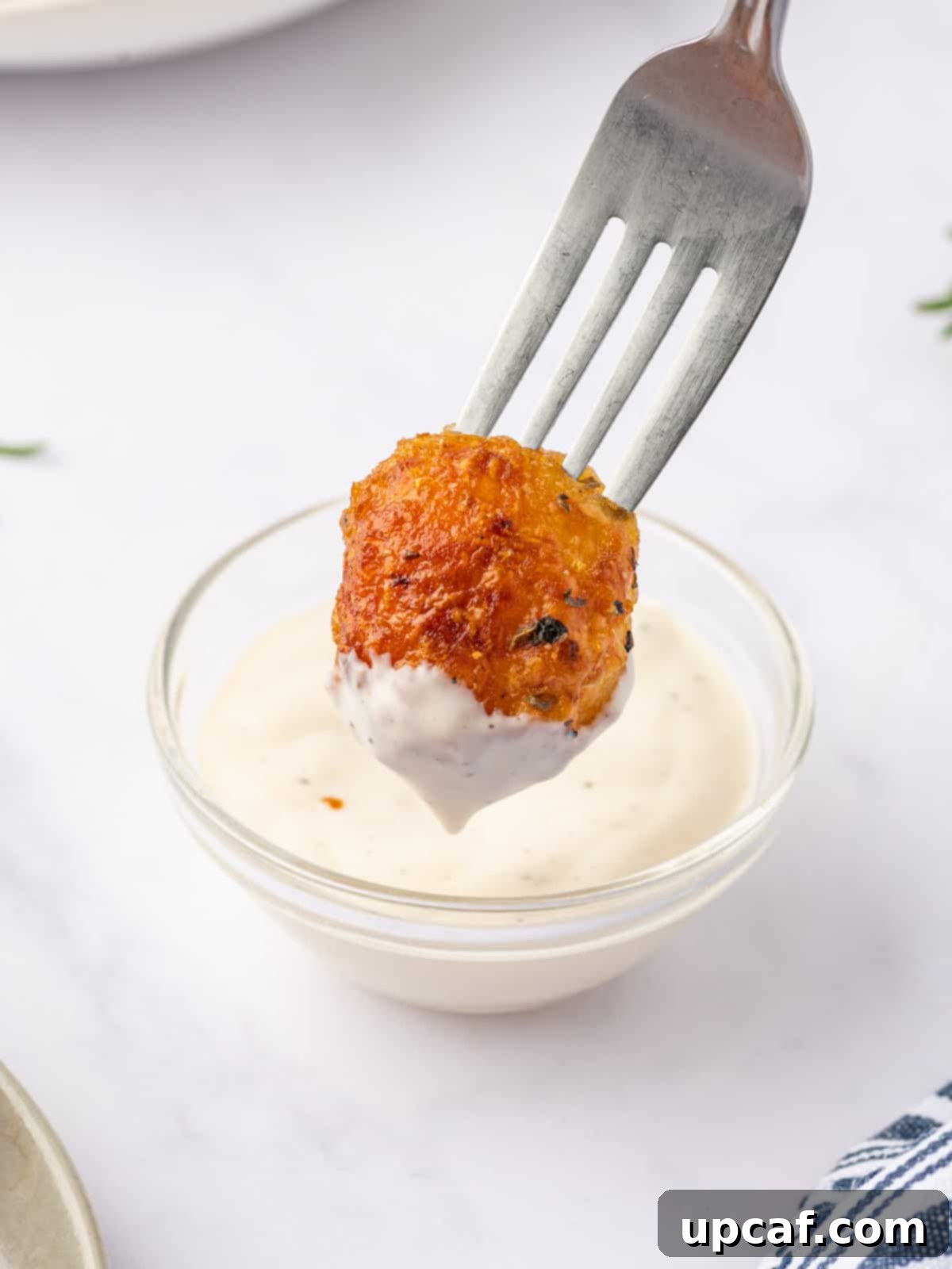A close-up of a crispy roasted baby potato being dipped into a creamy, savory sauce.