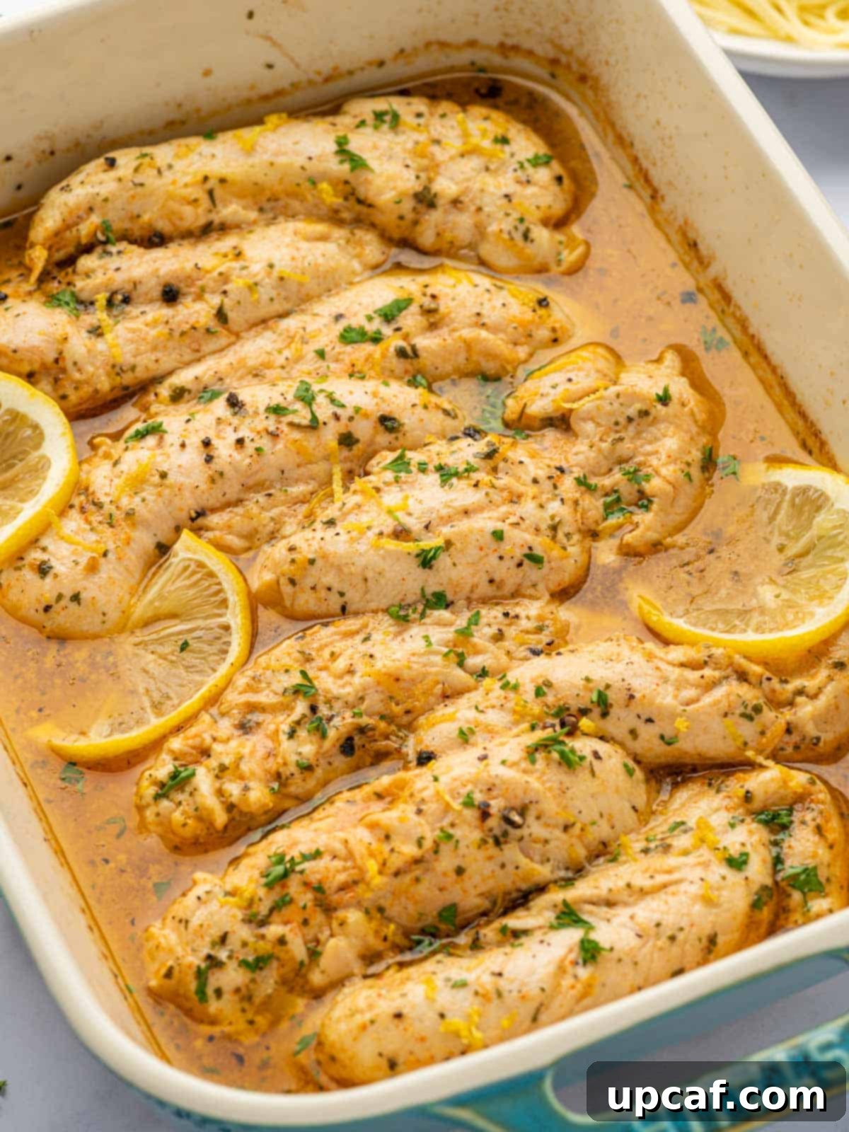 A baking dish with lemon pepper chicken tenders garnished with cilantro and lemon.
