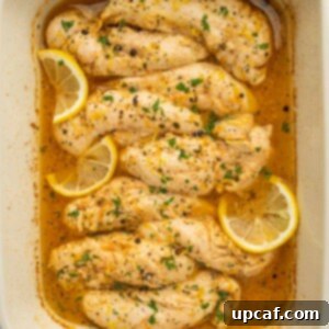 Lemon pepper chicken fingers baked in a dish and garnished with lemon.