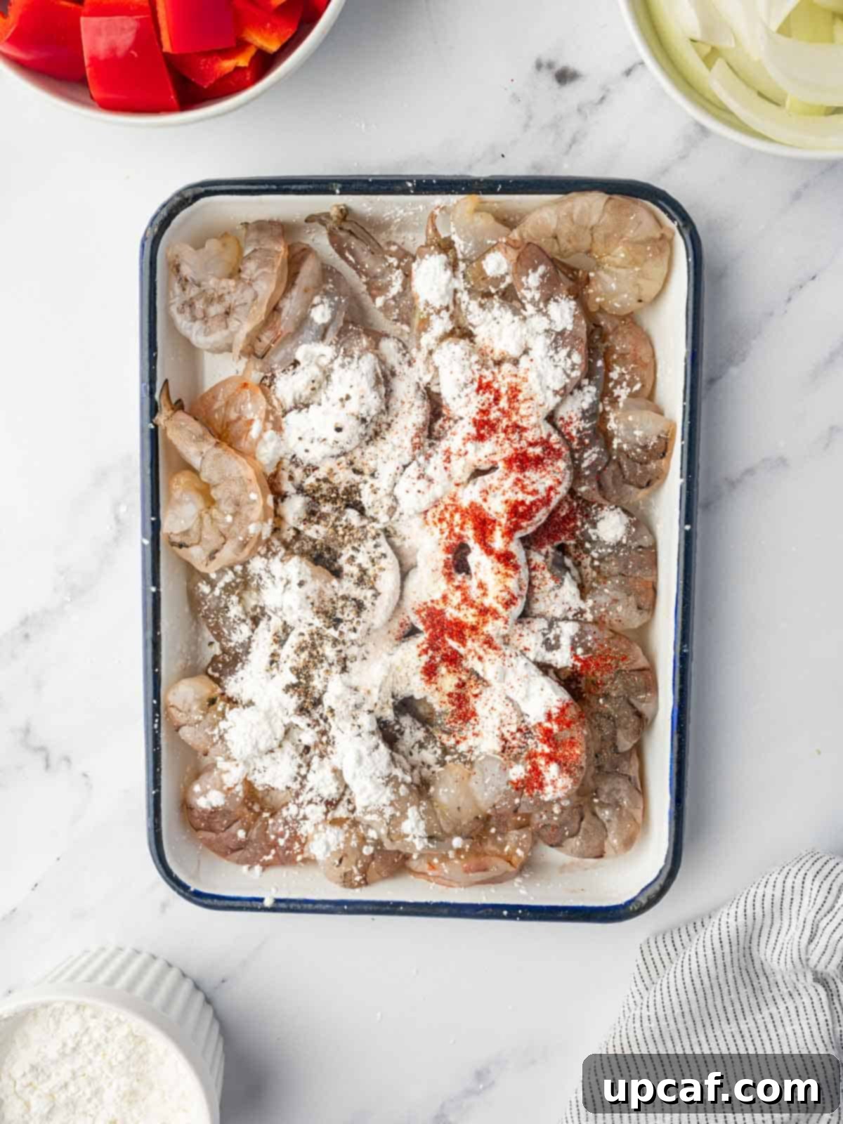 Shrimp being seasoned in a bowl with spices.