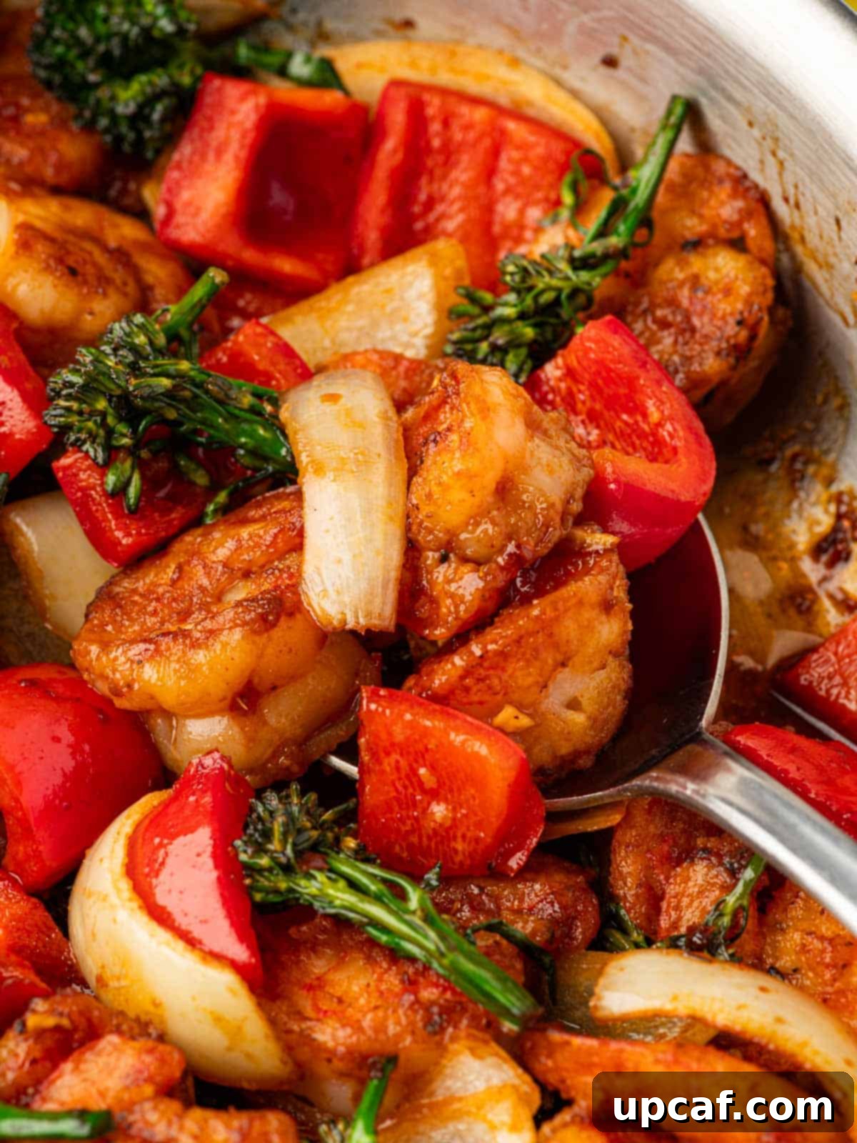 A spoon serving a generous portion of Sizzling Shrimp and vegetables from a skillet.