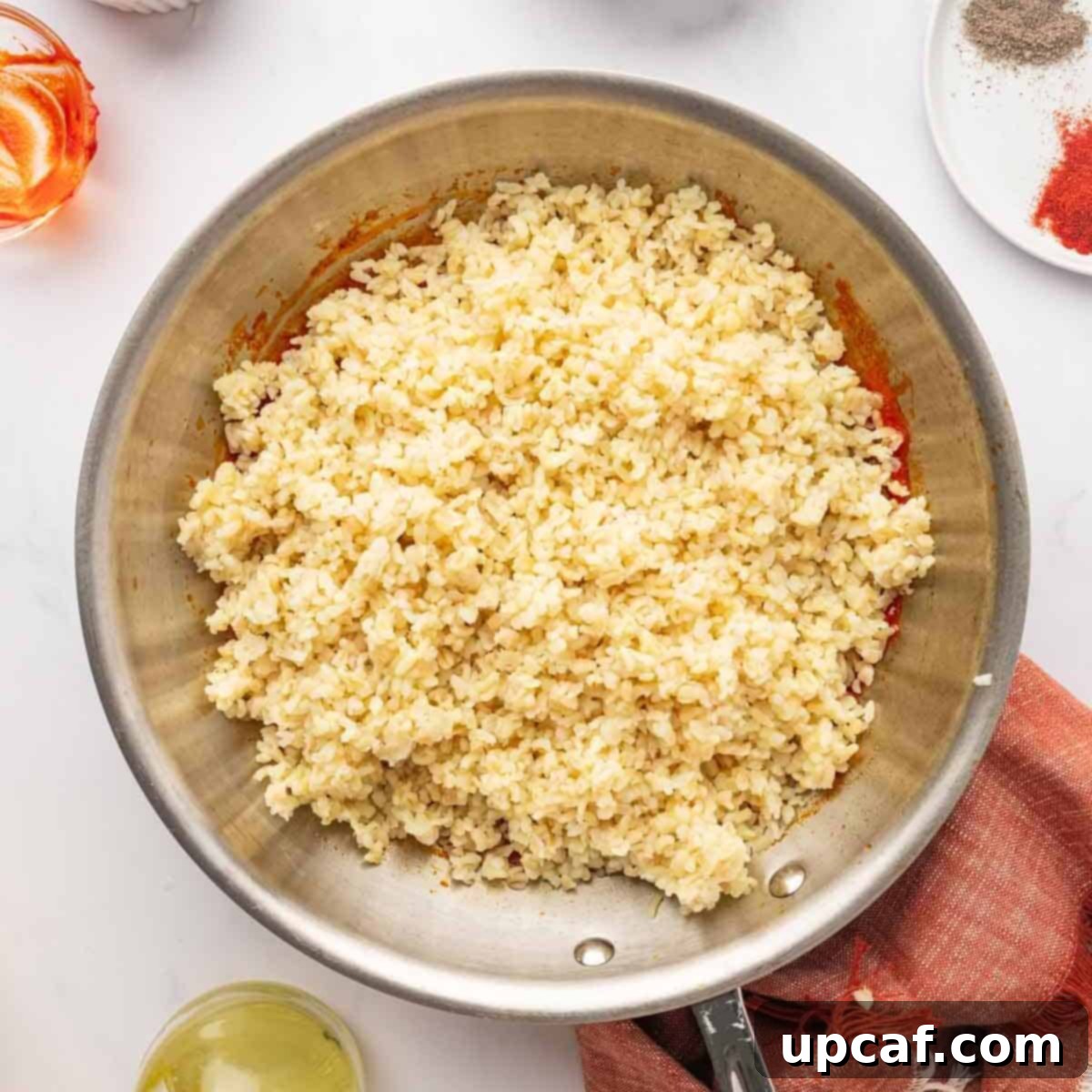 Fluffy, cooked bulgur wheat mixed with tomato and red pepper paste in a pan, before adding fresh vegetables.
