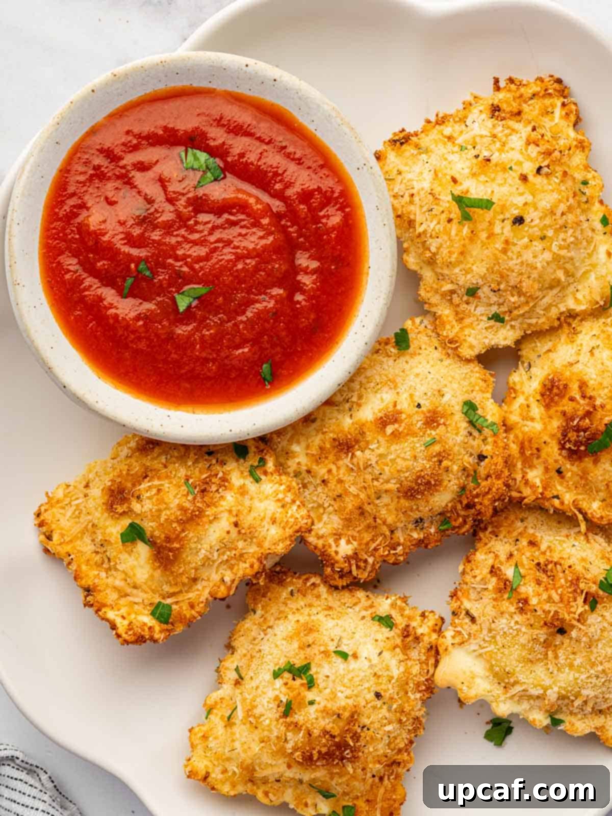 Air fried ravioli on a plate with a small bowl of marinara.