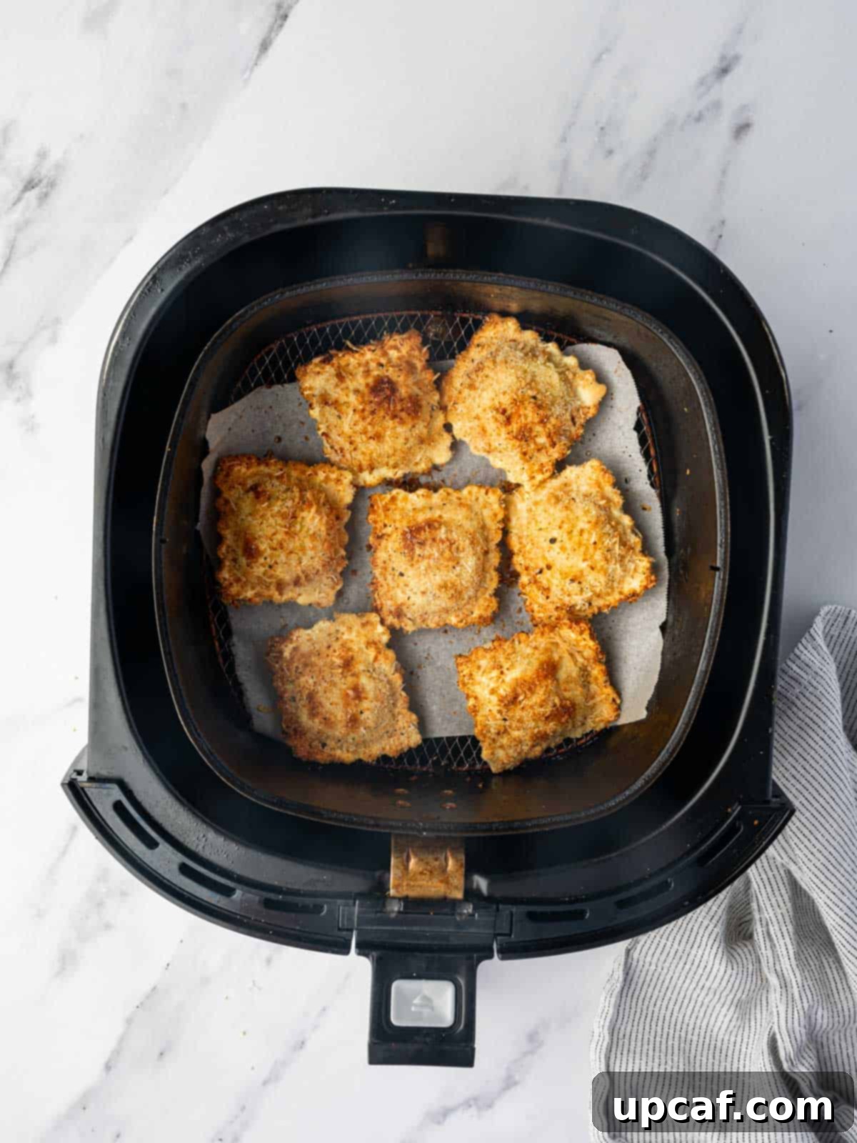 Air fryer basket with a single layer of air fried ravioli.