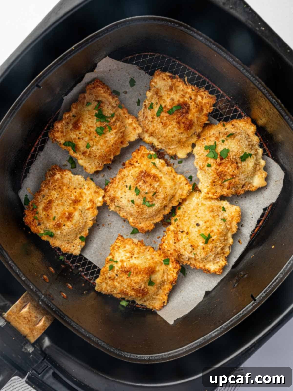 Air fried ravioli in an air fryer basket.