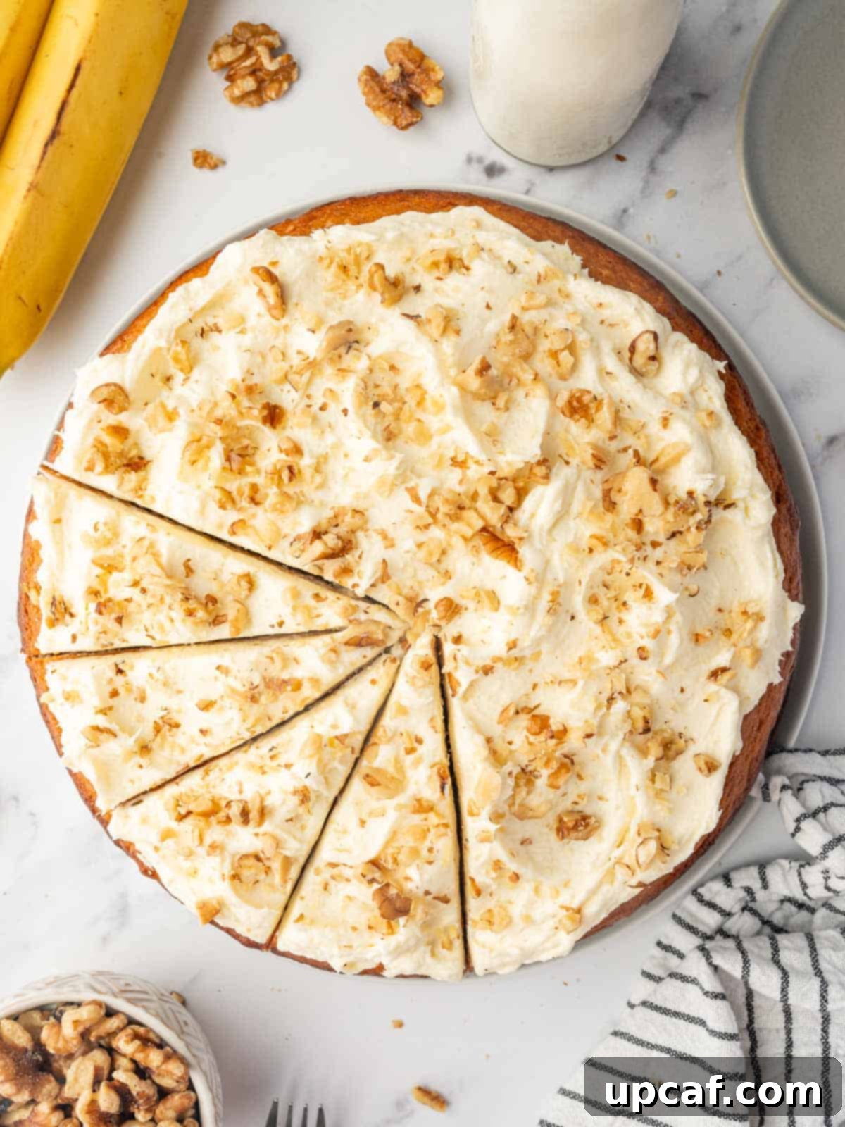 Slices are beautifully cut into a banana walnut cake, revealing its moist interior and generous distribution of walnuts and frosting.